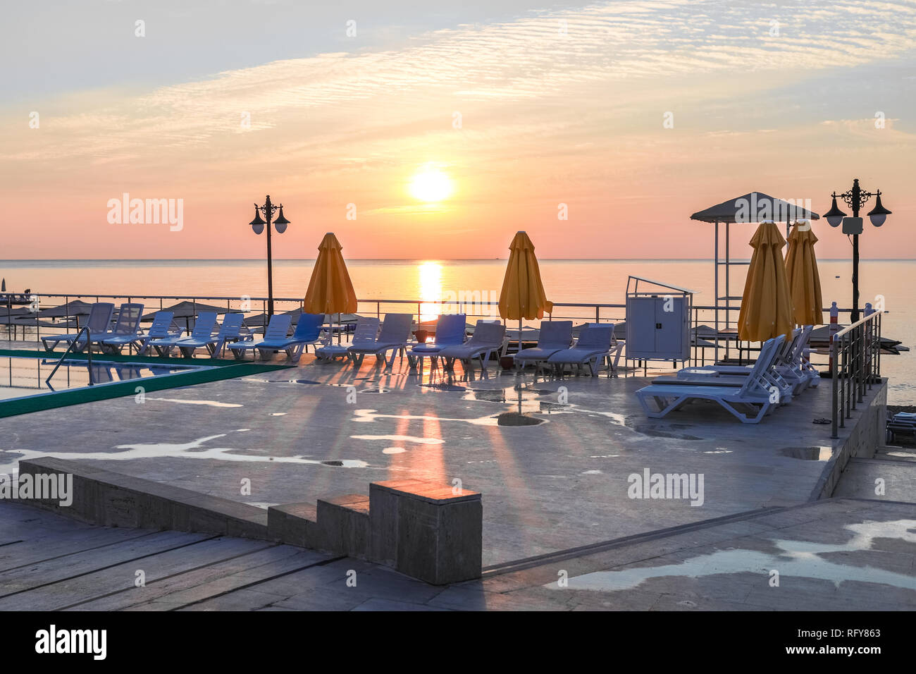 Sun rays are falling on concrete sunbathing area on seascape dawn background. Stock Photo