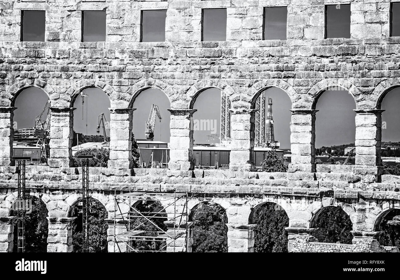 Pula Arena and cranes in a cargo port, Istria, Croatia. Travel destination. Ancient architecture. Black and white photo. Stock Photo