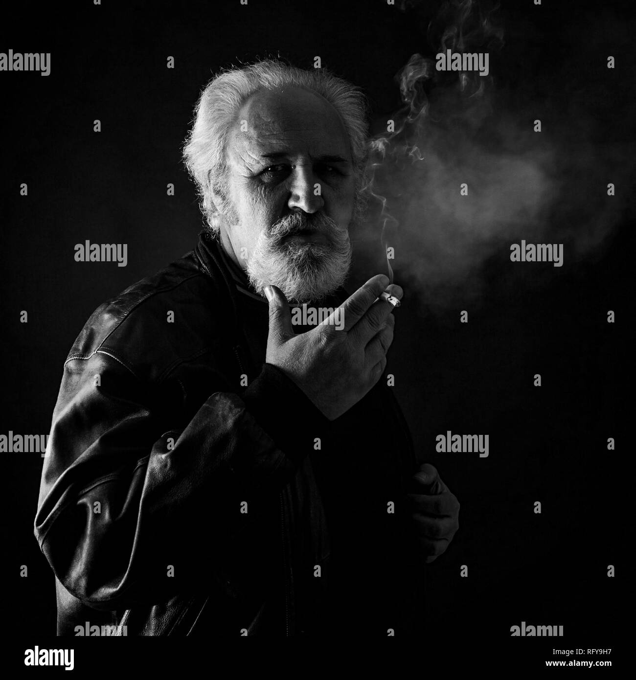 Grumpy man smoking against black background Stock Photo