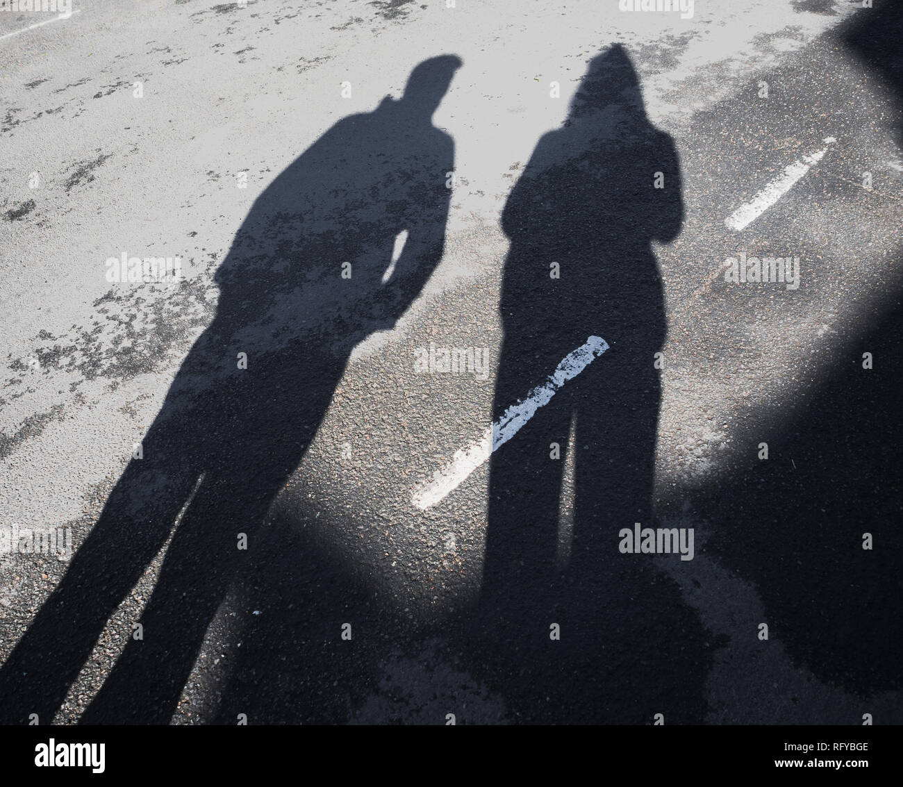 Long shadow of man and woman on asphalt road with dividing line outdoors. Stock Photo