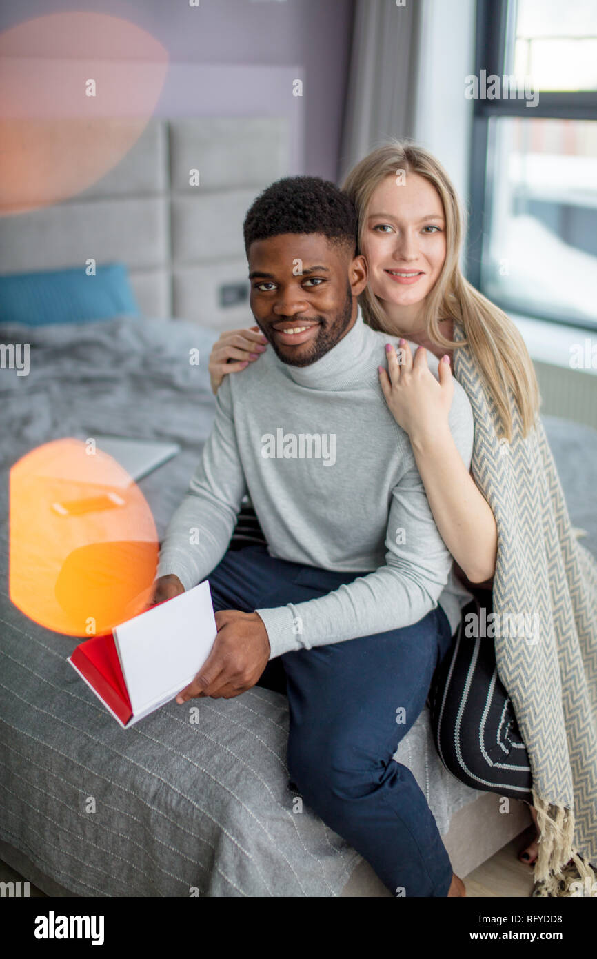 Happy interracial couple spending weekend together at home, relaxing with book Stock Photo