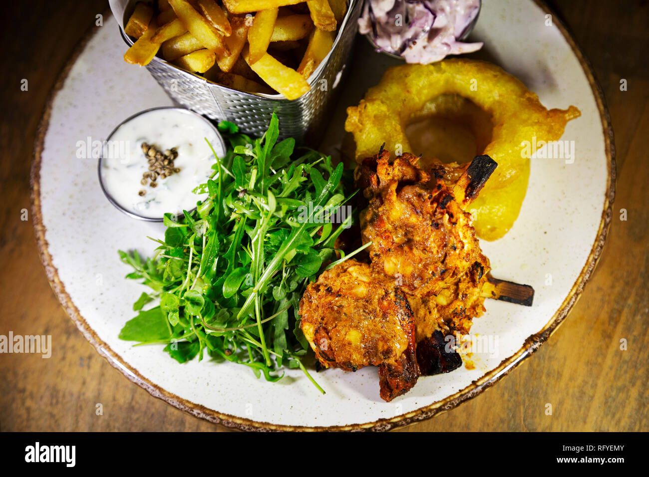 Grilled king prawns served with fries, onion rings and dips. The dish is garnished with rocket. Stock Photo
