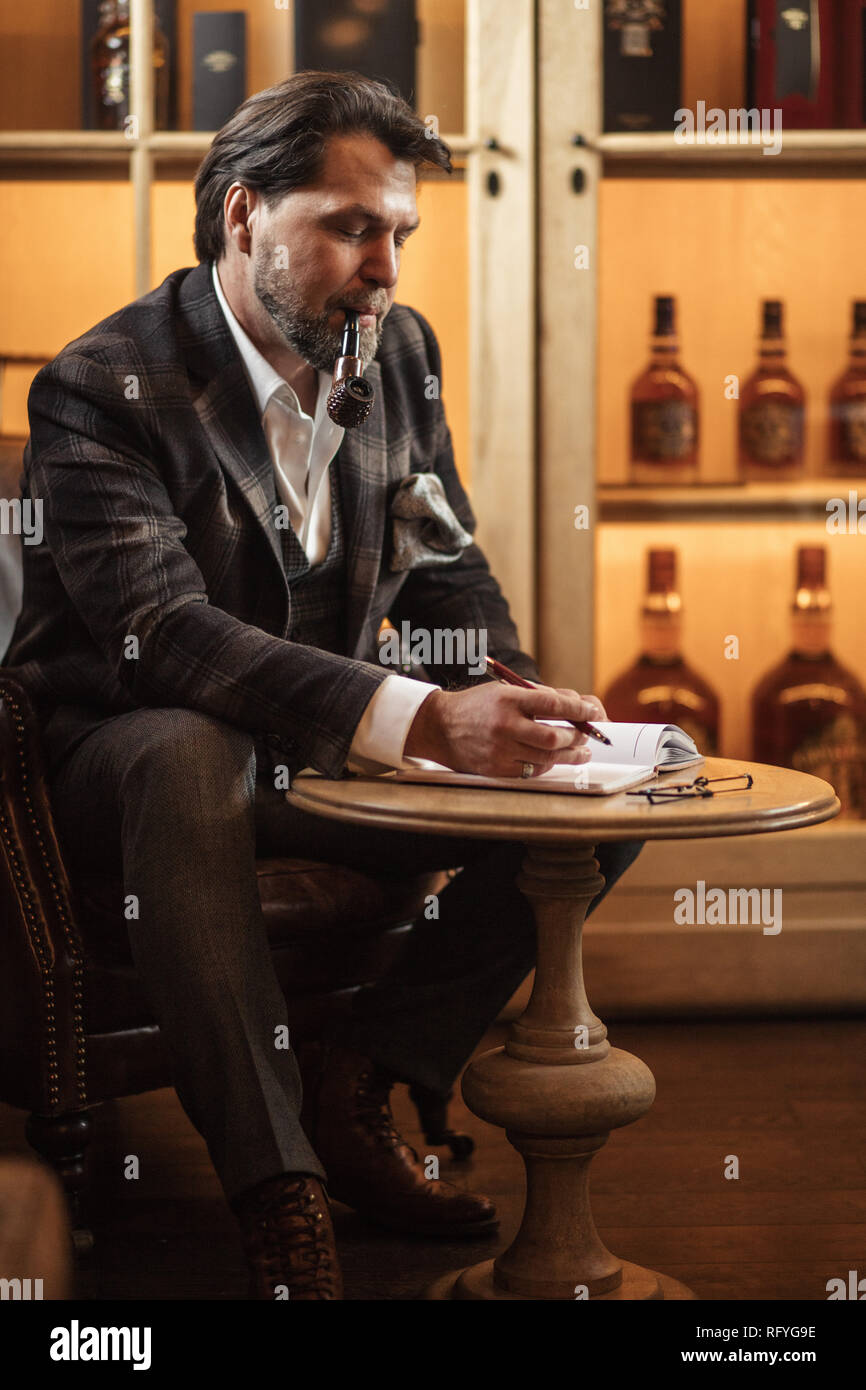 Talanted mature writer in trendy suit is making notes in diary or notebook. Stock Photo