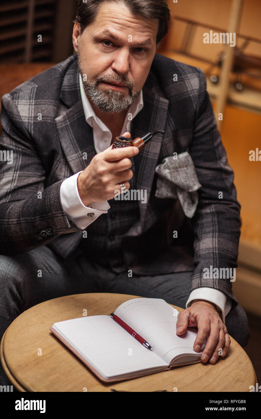 Talanted mature writer in trendy suit is making notes in diary or notebook. Stock Photo