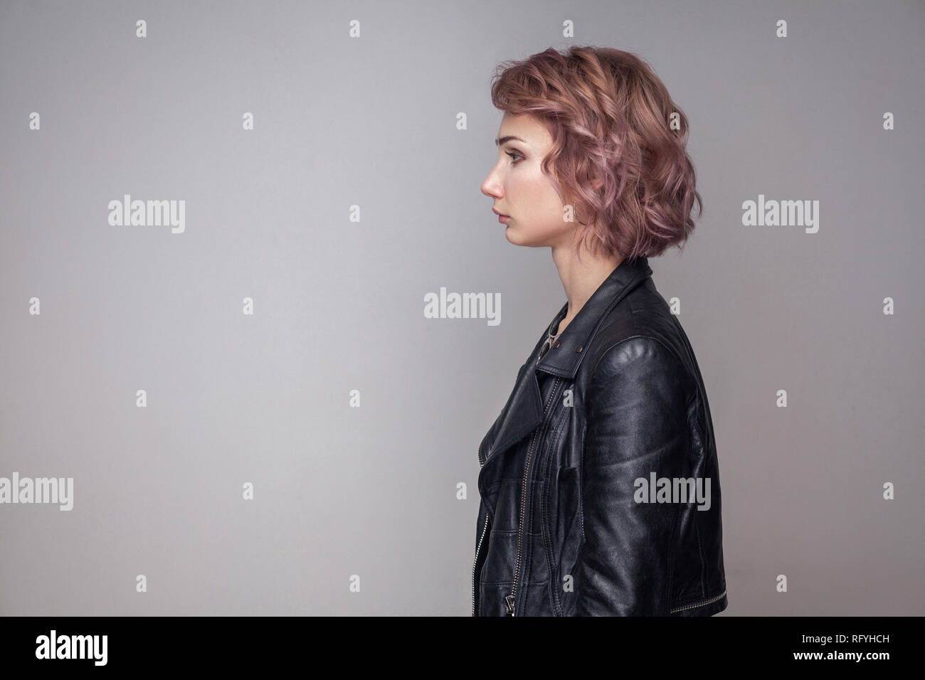 Profile side view portrait of serious beautiful girl with short hairstyle and makeup in casual style black leather jacket standing and looking aside.  Stock Photo