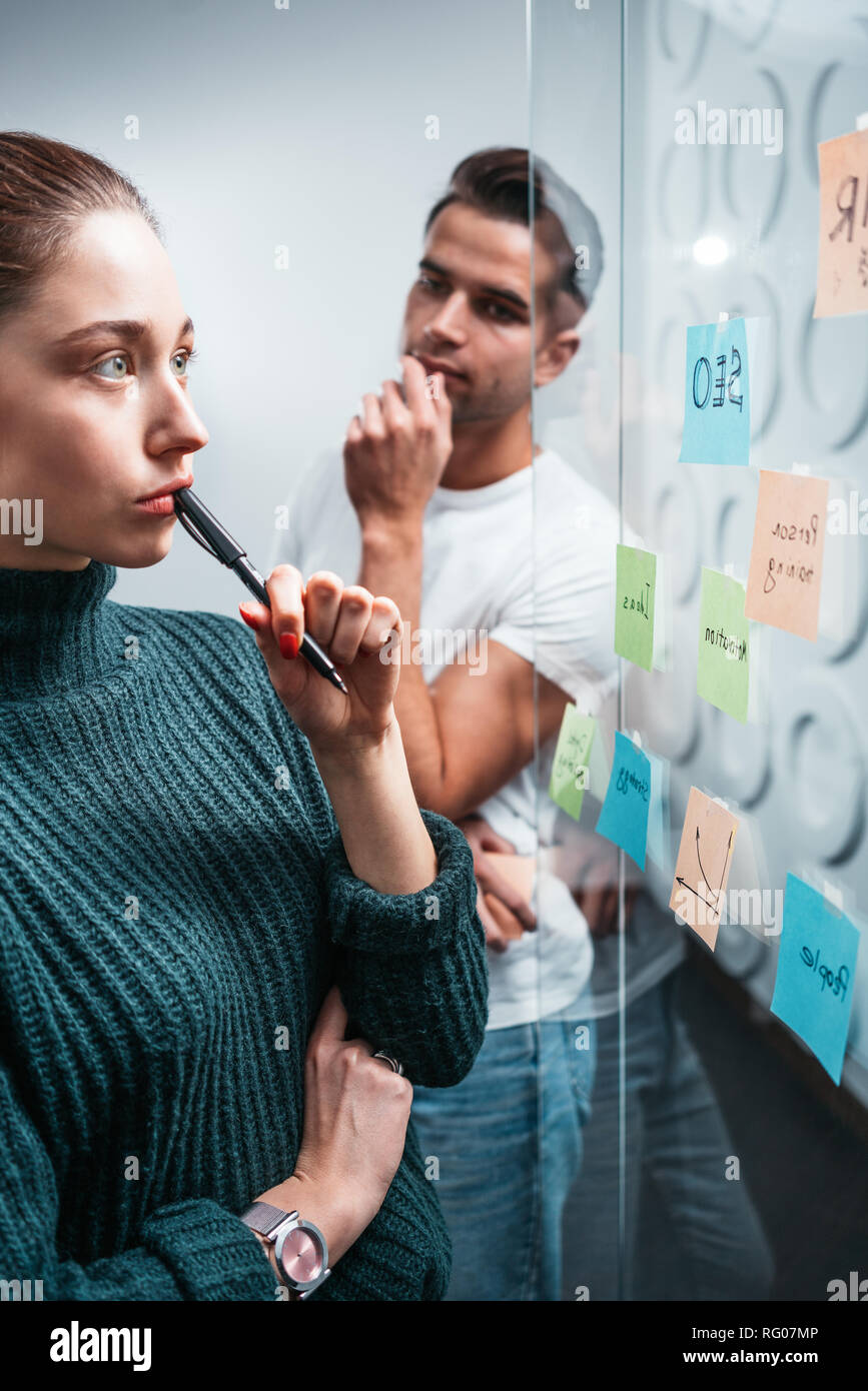 Portrait of coworker people standing at office space behind glass wall with sticky notes. Team of manager disscusing and brainstorming new sturtup ide Stock Photo