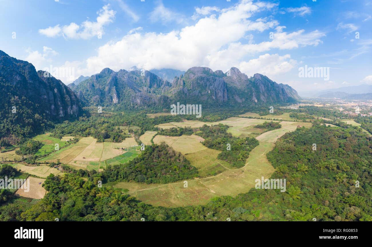 Aerial: Vang Vieng backpacker travel destination in Laos, Asia. Dramatic sky over scenic cliffs and rock pinnacles, rice paddies valley, stunning land Stock Photo