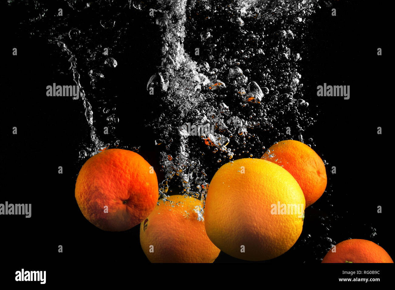 Clementines falling in water with splash on black background Stock