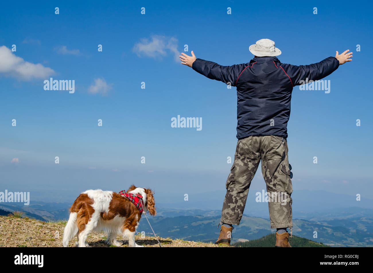 Man with spread arms in a joyful pose, with his dog in a mountain landscape Stock Photo