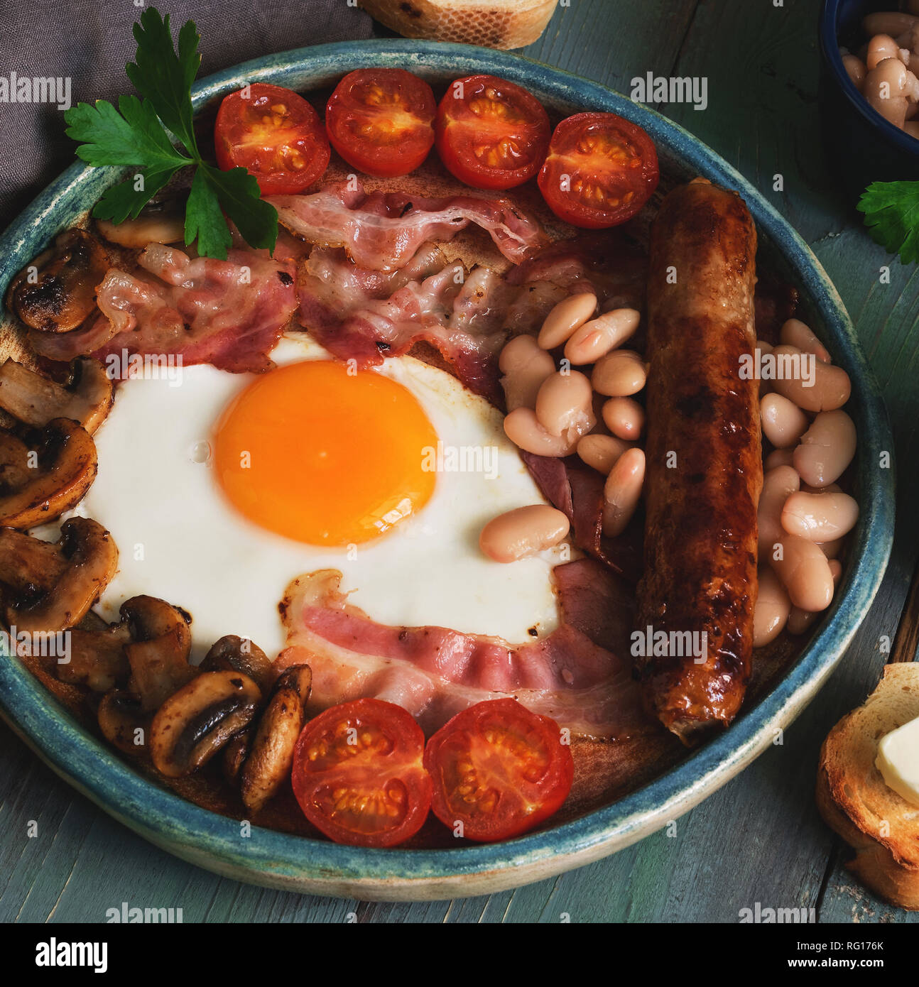 Traditional English breakfast, scrambled eggs, bacon, mushrooms, sausage, beans and cherry tomatoes on a rustic plank table. Selective focus Stock Photo