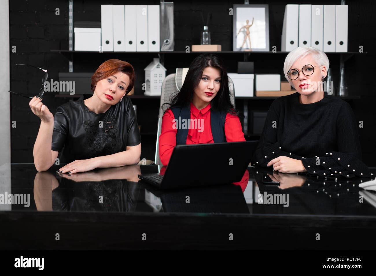 Three female colleagues sitting in office at table with laptop Stock Photo