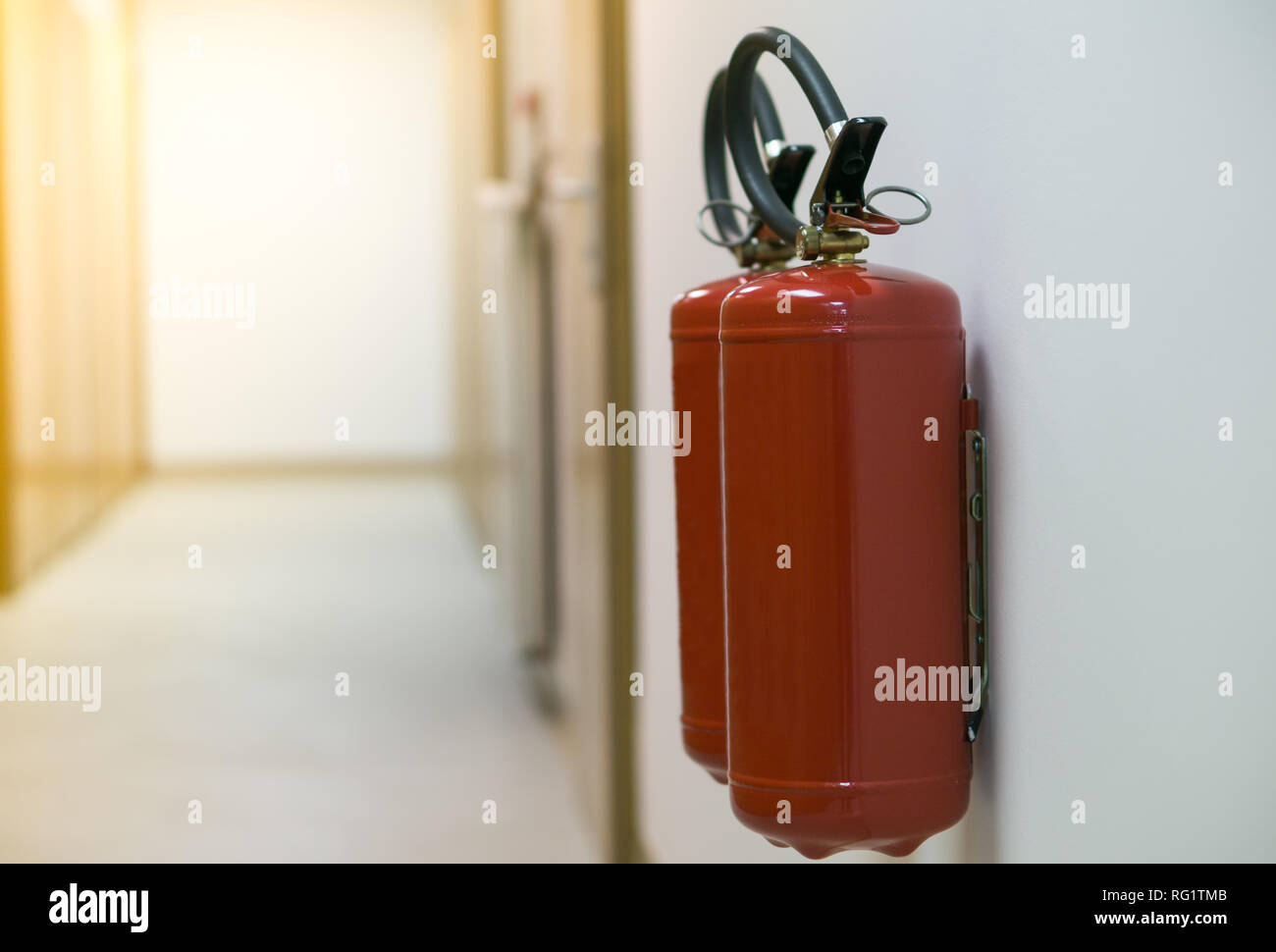 Red fire extinguisher in empty corridor on the white wall with sun