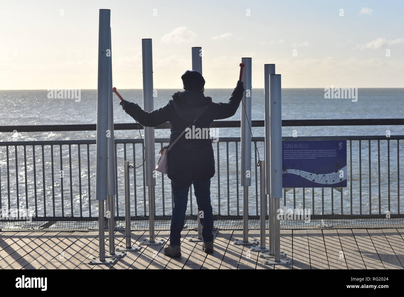 Woman playing tubular bells at the end of the pier, Boscombe, Bournemouth, Dorset, UK, 27th January 2019, Weather: Winter sunshine and windy on the pier. A temperature of just 5 degrees mid-morning is made to feel even colder by the wind chill from strong winds gusting to 50mph. Stock Photo