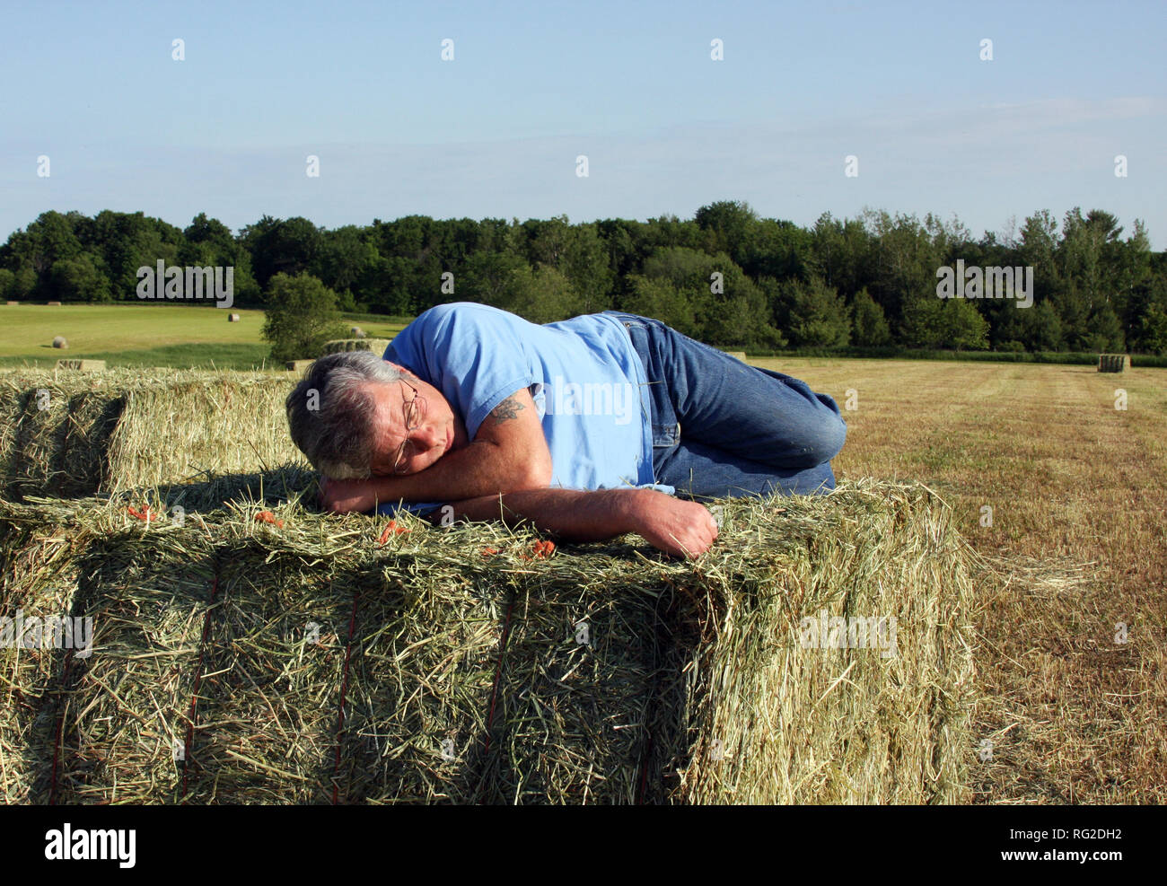 Man sleeping on a hay bale with the field and sky in the background Stock Photo