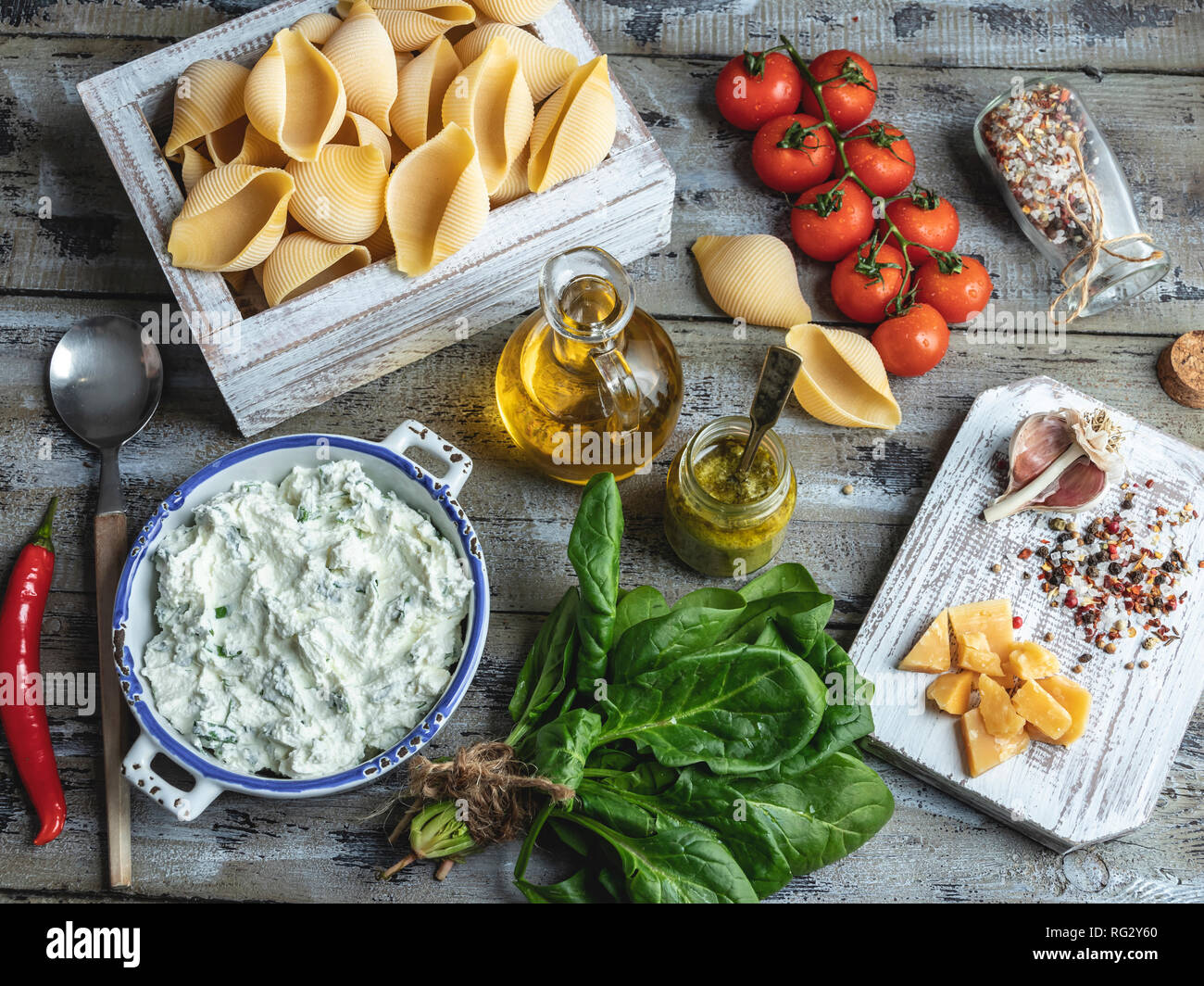 Ingredients for cooking pasta. Conchiglioni, spinach leaves, cherry tomatoes, parmesan cheese, cream cheese, olive oil, salt, garlic, rustic style, wo Stock Photo
