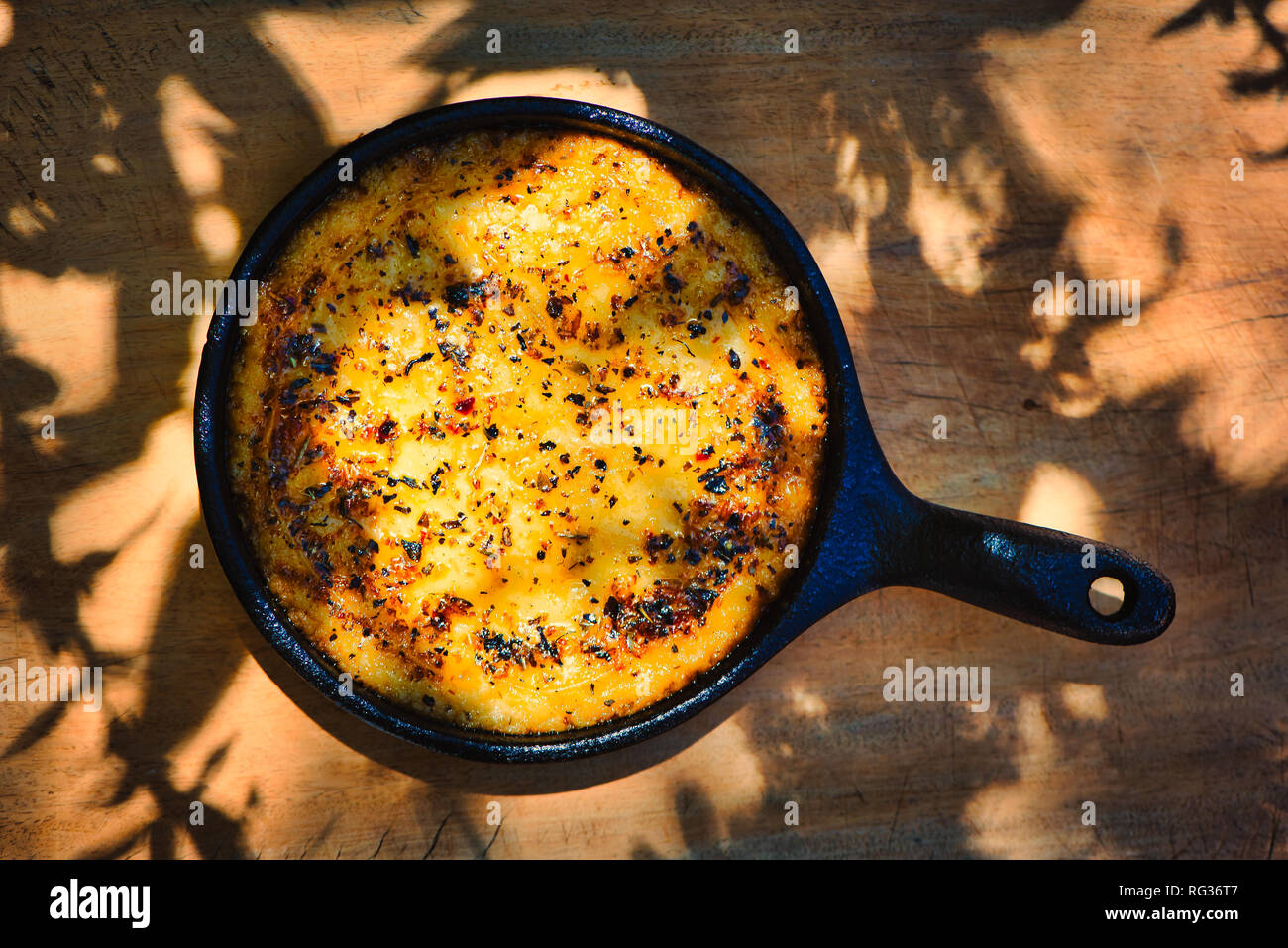 Delicious Argentinian Provolone Yarn Cheese (Provoleta) that was cooked in a cast iron skillet over the embers presented on an old wooden board. Stock Photo