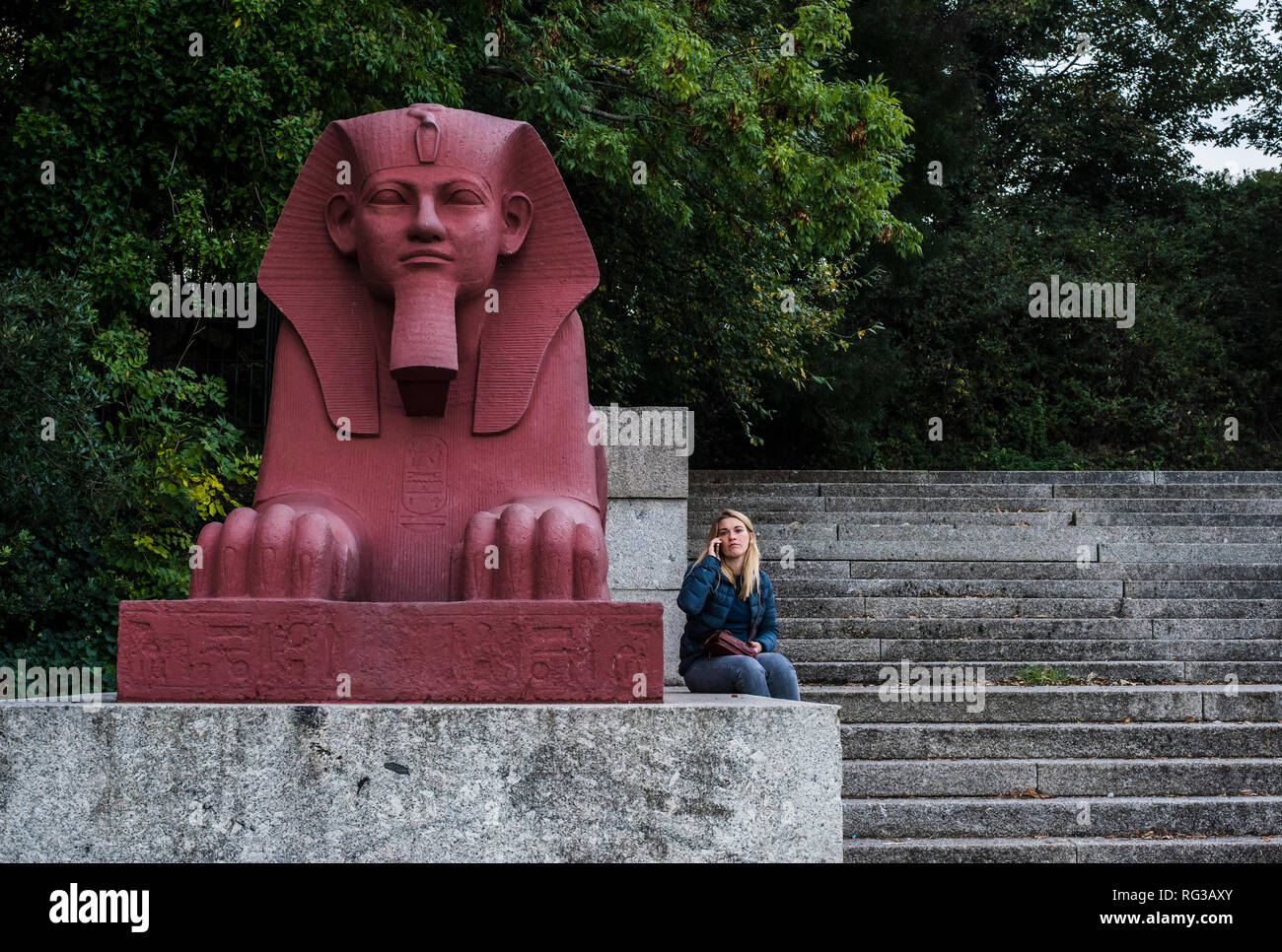 Woman, using smartphone, sitting beside painted terracotta sphinx, part of the grand terrace, Crystal Palace, London, England, UK Stock Photo