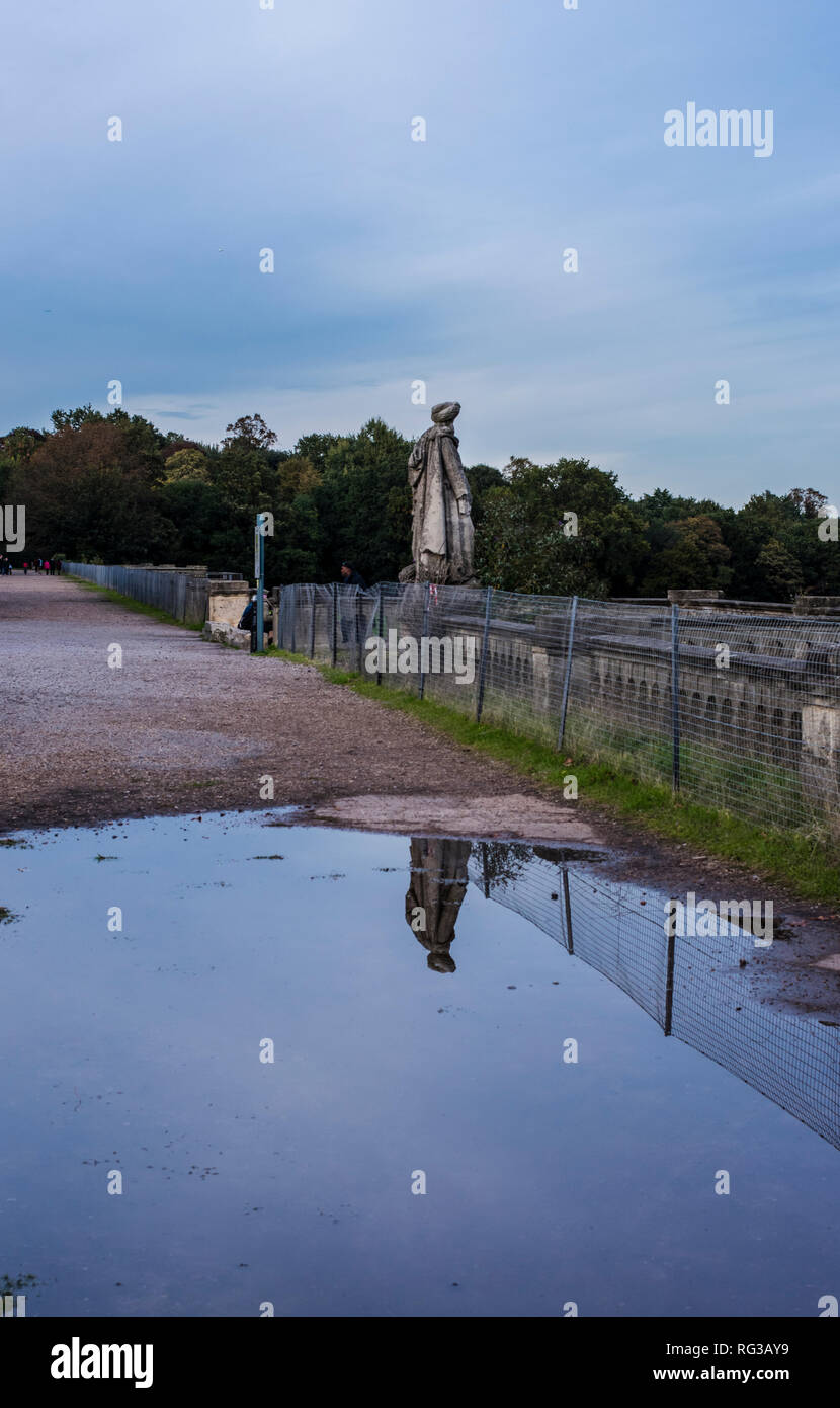 Statue (one of the few to still have its head) reflected in water, rear view, Crystal Palace park, Crystal Palace, London, England, UK Stock Photo
