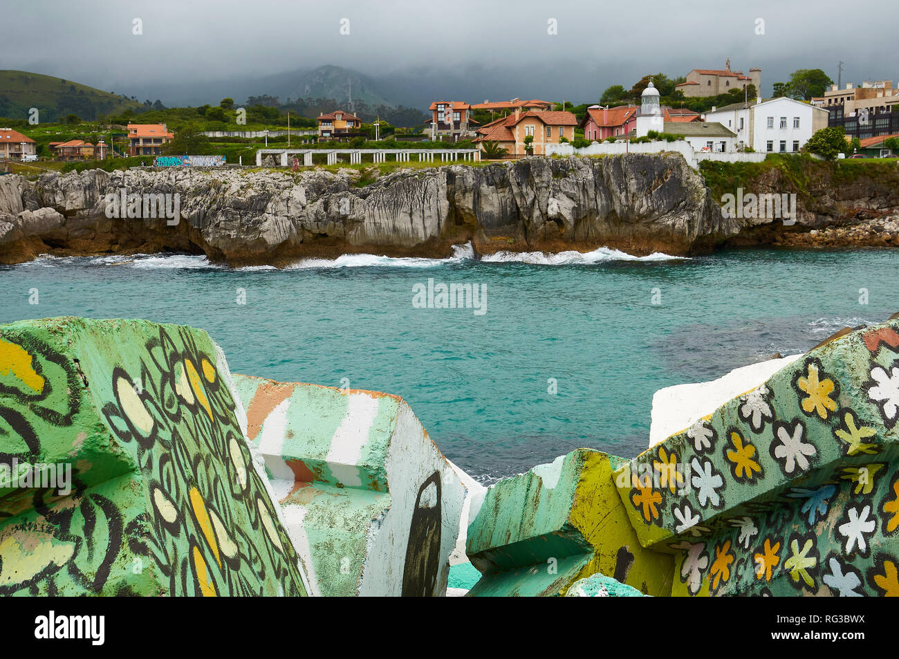 Cubos de la Memoria, artistic intervention from Agustín Ibarrola of painted concrete blocks with town in the back in Llanes harbour (Asturias, Spain) Stock Photo