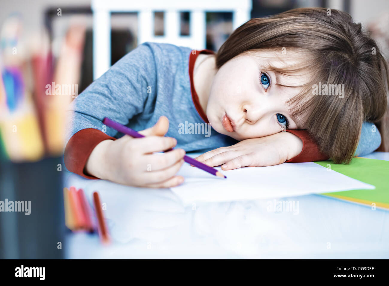 Portrait Kid girl holding colour pencil sitting alone and looking out with bored face, Preschool child laying head down on table with sad face Stock Photo