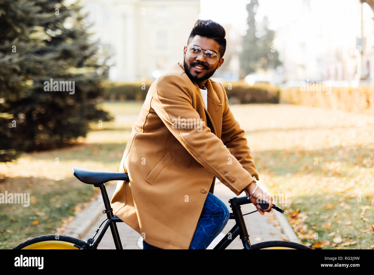 Young bearded indian man in coat while sitting on his bicycle outdoors Stock Photo