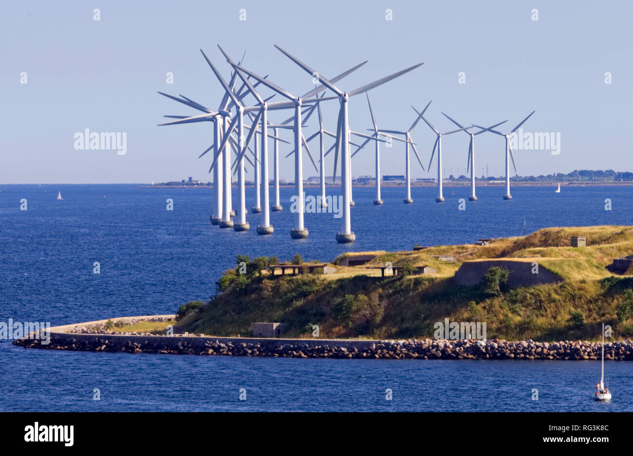 Copenhagen's Energy producing white windmills line along an island by the ocean Stock Photo