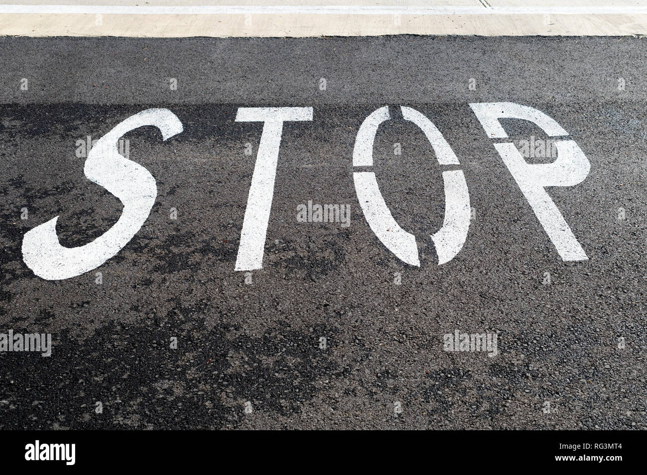 stop, painted on a black tarmac road. Stock Photo