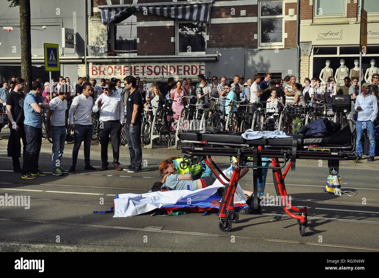 View of a young female casualty lying on the tram tracks after an accident, surrounded by ambulance service employees and passersby. Stock Photo