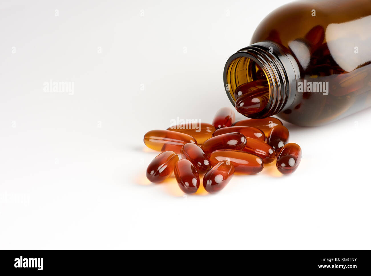 Close-up view of orange pills or lecithin capsules in a brown glass bottle on a white background with space for text Stock Photo