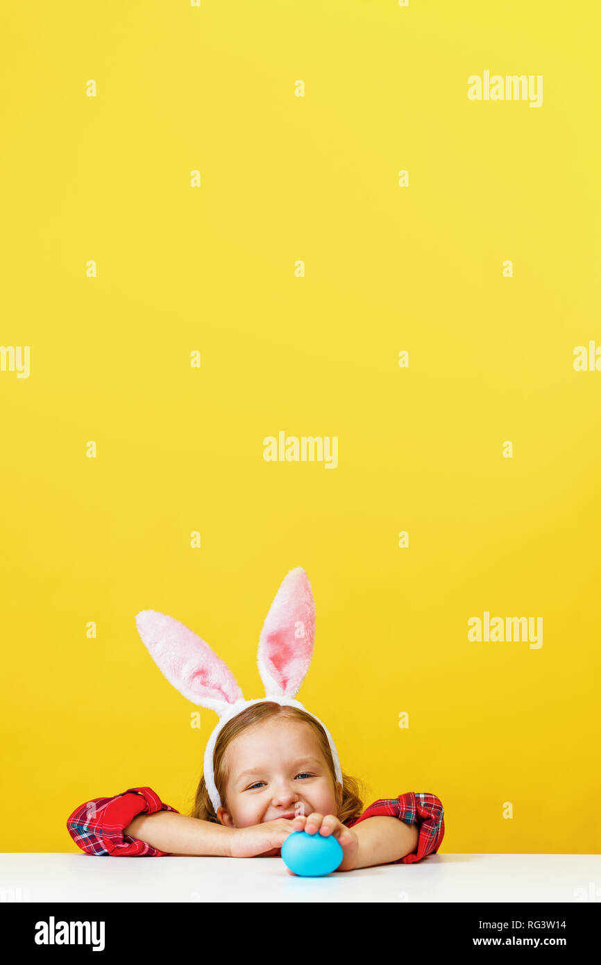 Cute little child girl with bunny ears at home is hunting for Easter eggs. Stock Photo