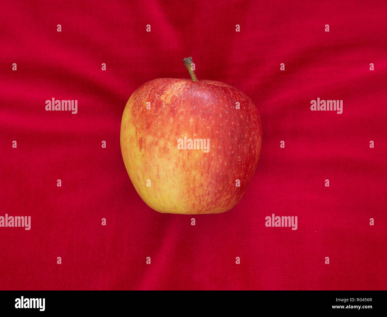 Apple on red velvet cushion, temptation or luxury, with copyspace. Stock Photo