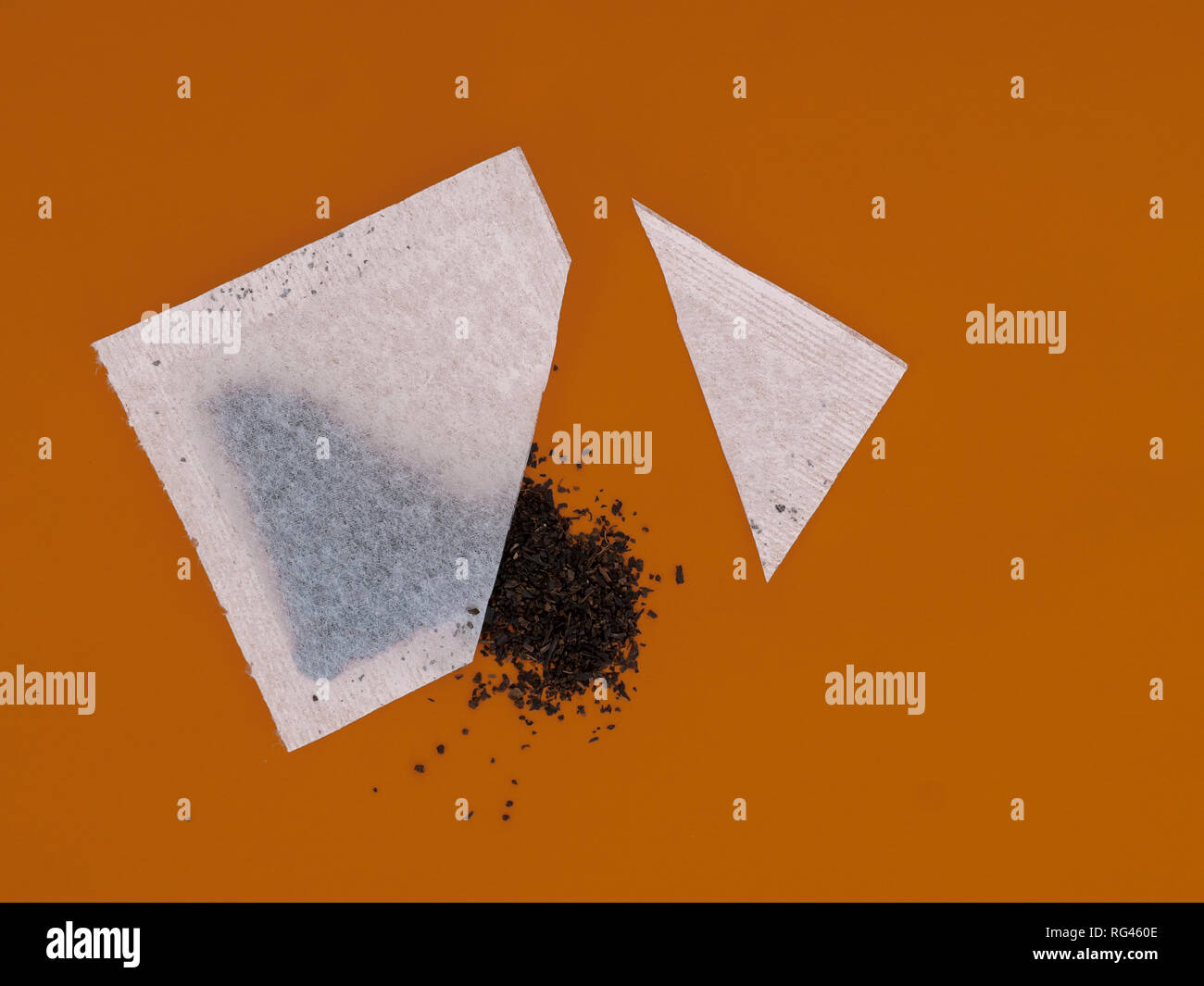 Tea bag sachet cut open to see contents and quality of leaves inside, on orange colour background. Stock Photo