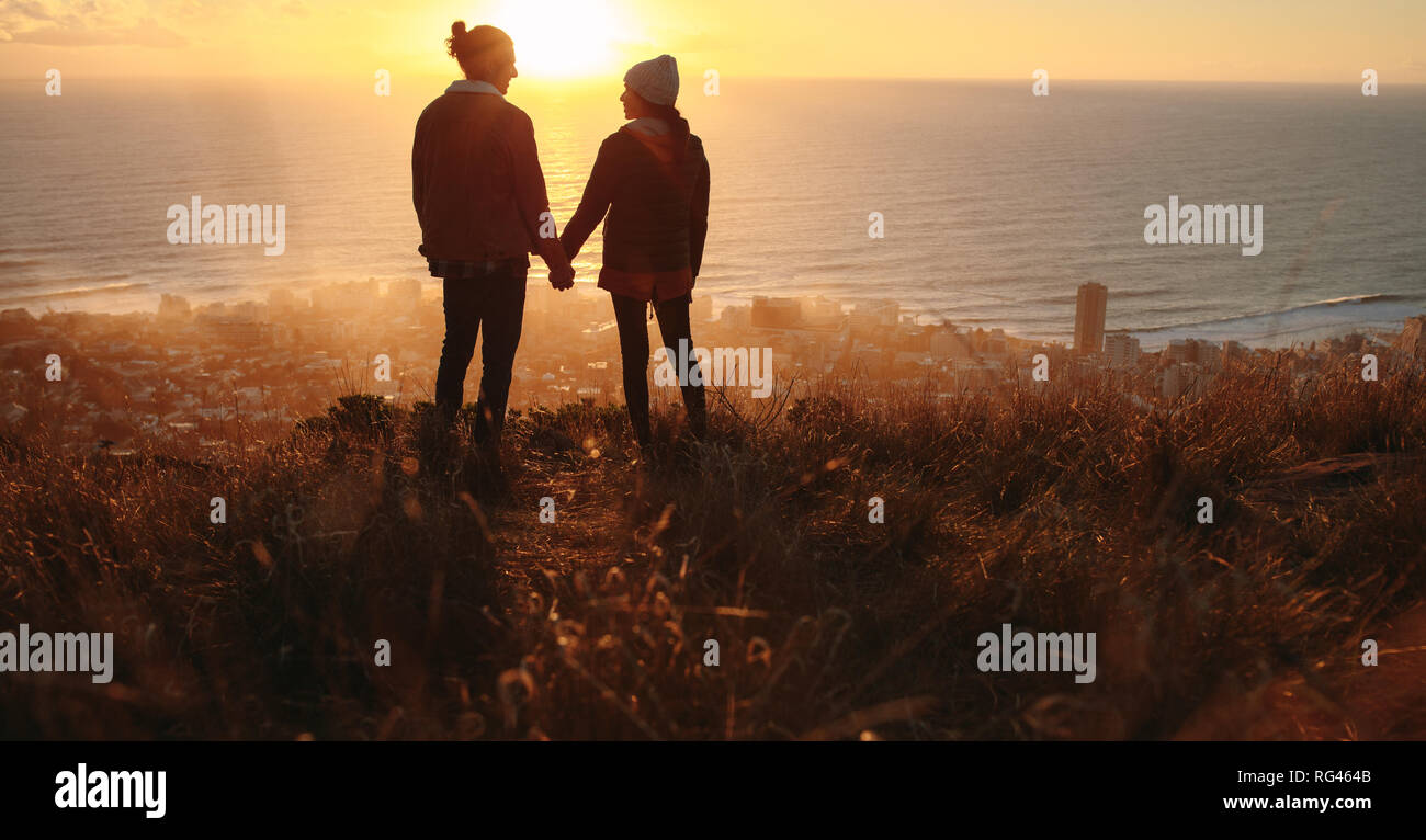 Silhouette of young man and woman in love standing on the mountain peak ...