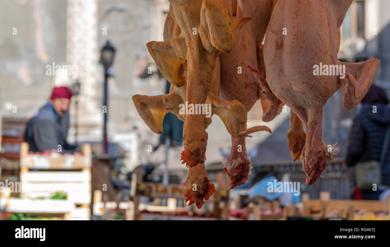 Plucked chickens hanging upside down. In background out of focus food market Stock Photo
