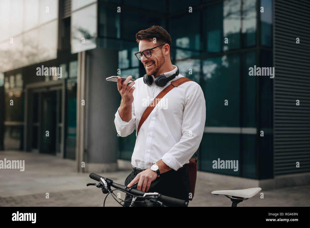 Man talking on mobile phone on loudspeaker standing on street with his bike. Businessman standing on street with bike talking on cell phone. Stock Photo