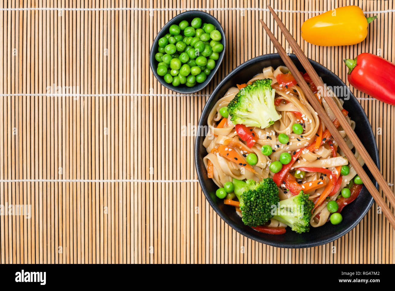 Asian noodle stir fry with vegetables and beans in bowl on bamboo background. Top view Stock Photo