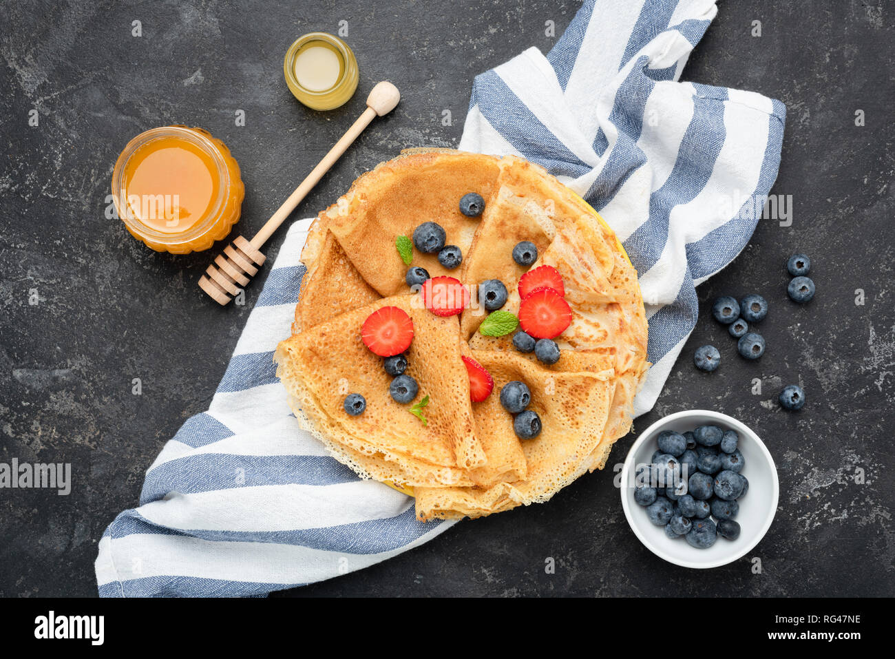 French Crepes or Russian Blini with berries, honey. Table top view, black concrete background Stock Photo