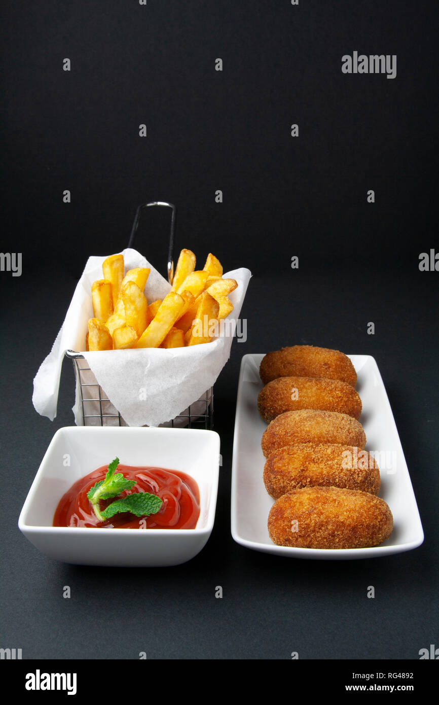 Gourmet ham and chicken croquettes with fried tomate and chips on dark
