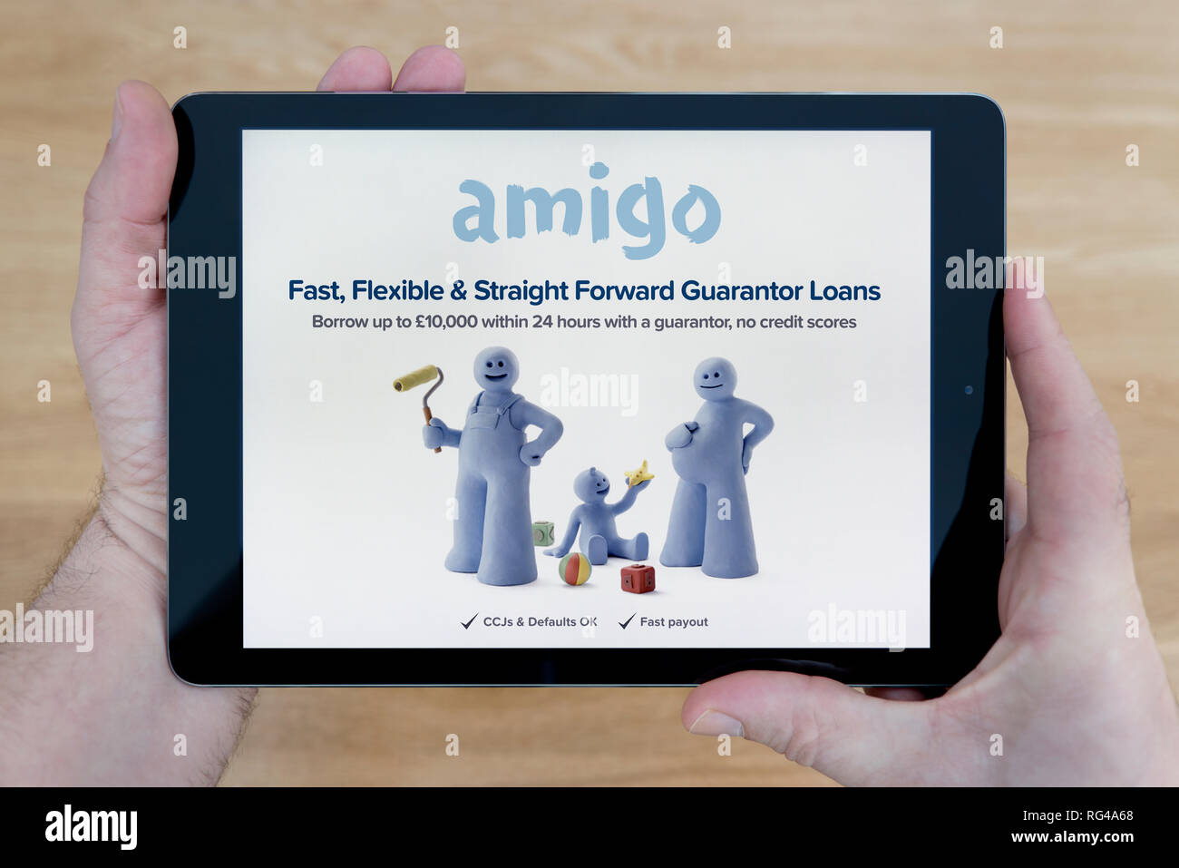 A man looks at the Amigo Loans website on his iPad tablet device, shot against a wooden table