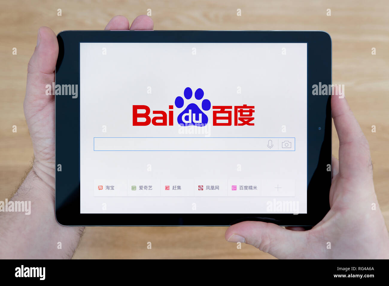 A man looks at the Baidu website on his iPad tablet device, shot against a wooden table top background (Editorial use only). Stock Photo