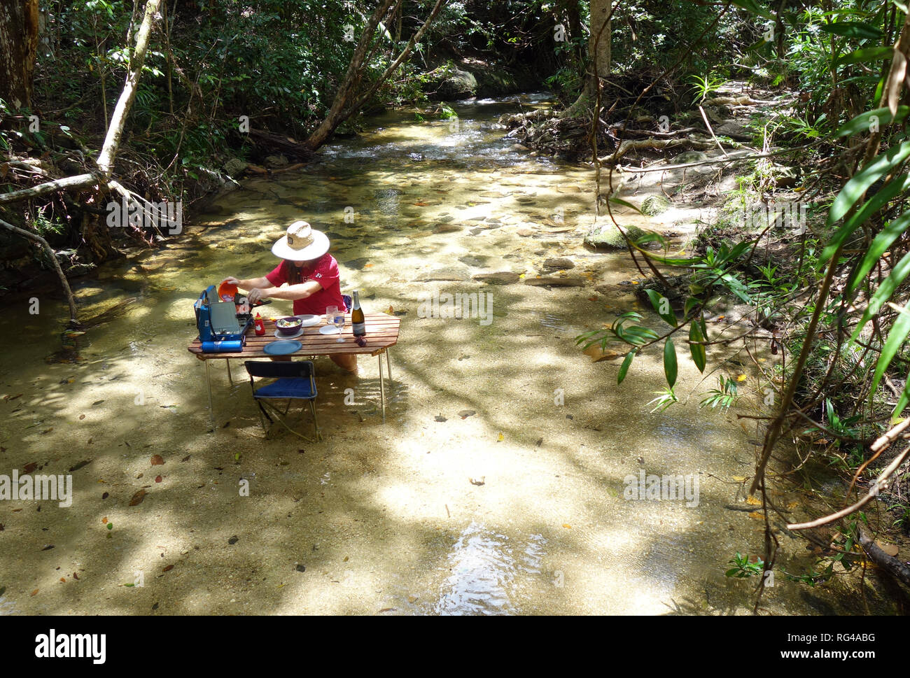 Man BBQing on picnic table set up in rainforest creek, Dinden National Park, near Cairns, Queensland, Australia. No MR or PR Stock Photo
