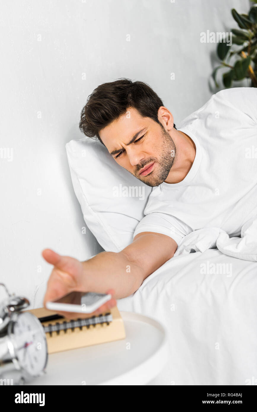 confused man waking up and looking at smartphone in the morning Stock