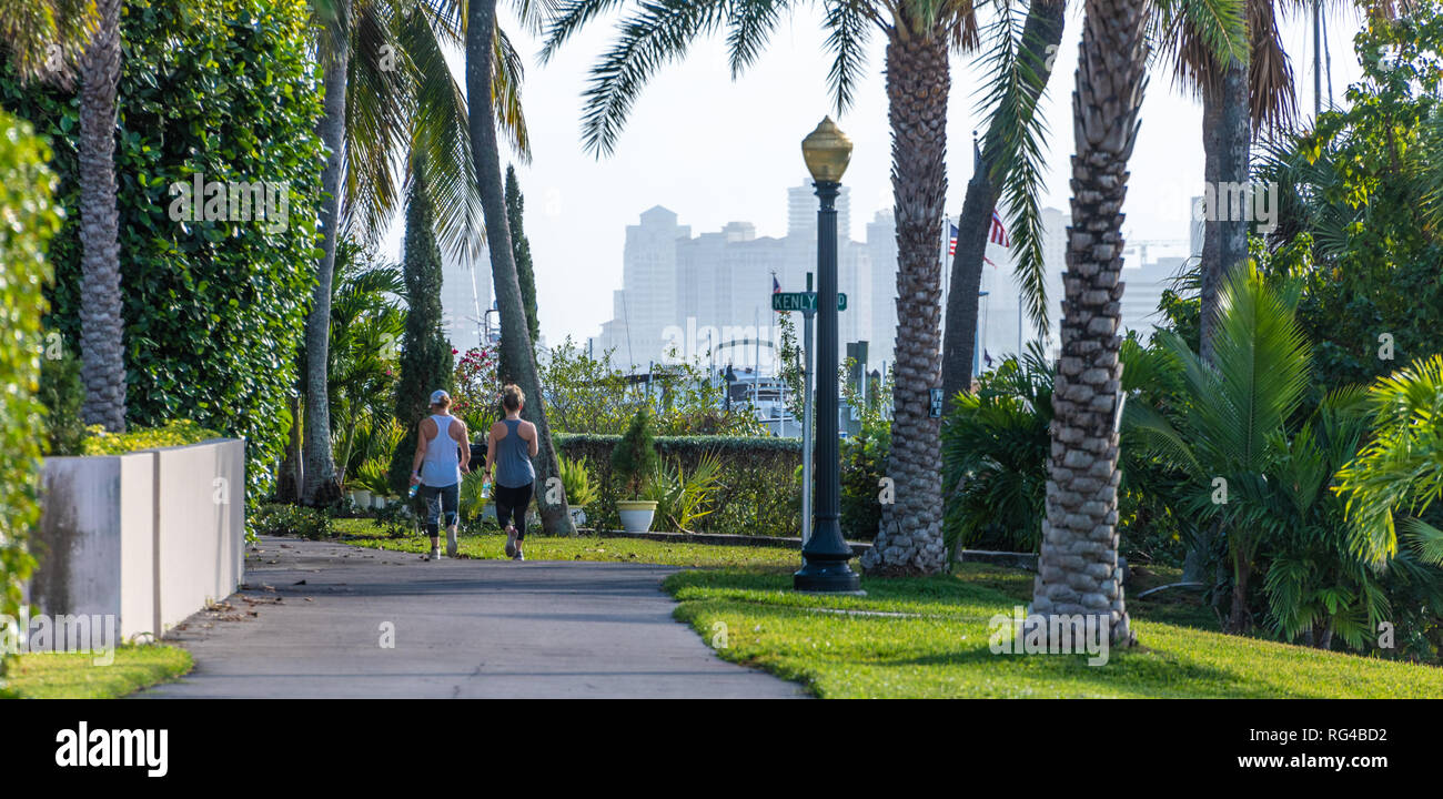 Two women walking along the Palm Beach Lake Trail in Palm Beach, Florida, with West Palm Beach in view across the Intracoastal Waterway. (USA) Stock Photo