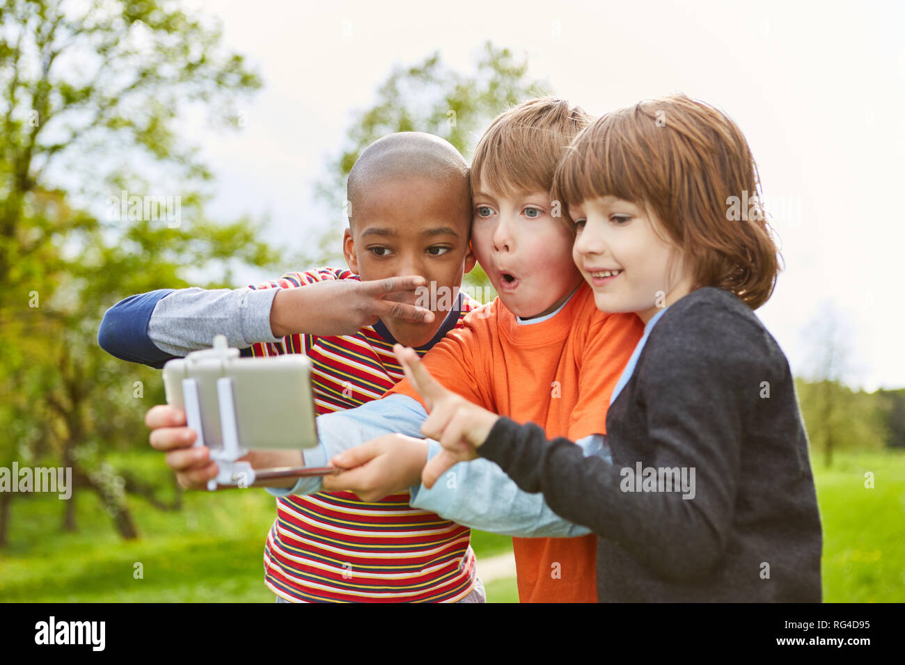 Three kids making faces for a selfie photo with their smartphone on the Selfie Stick Stock Photo