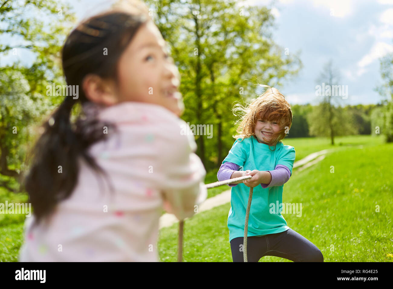 Two girls enjoy tug-of-war in the park in summer and measure their strength Stock Photo