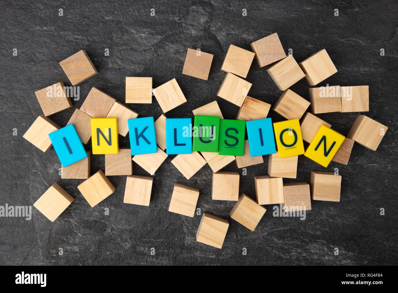 Concept: Inklusion means inclusion with colorful Toy Letters and wooden cubes on dark background Stock Photo