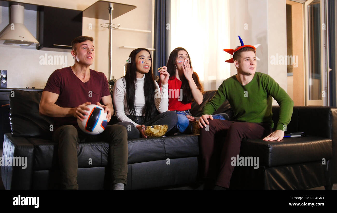 Four Young People Sitting On The Sofa And Watching Tv Wearing