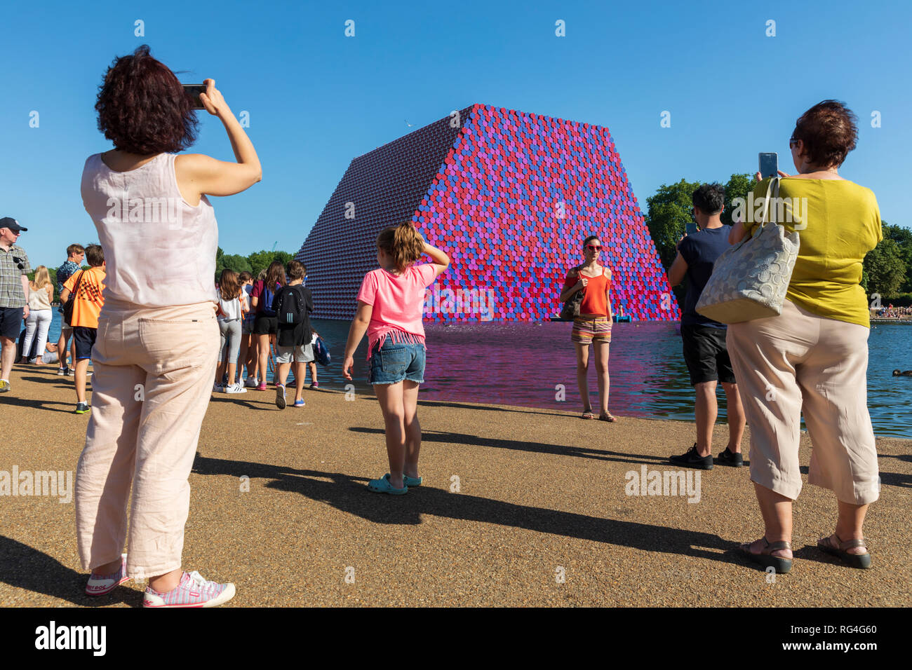 Tourists taking pictures in front of The London Mastaba sculpture by the artists Christo and Jeanne-Claude on the Serpentine Lake, Hyde Park, London. Stock Photo
