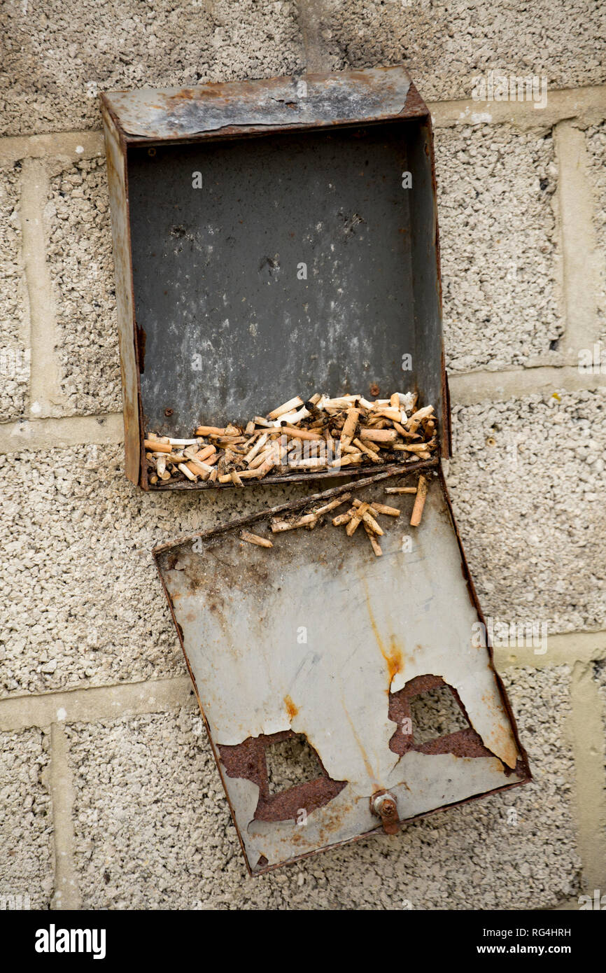 A broken cigarette bin with used cigarettes in it outside a social club. Dorset England UK GB Stock Photo