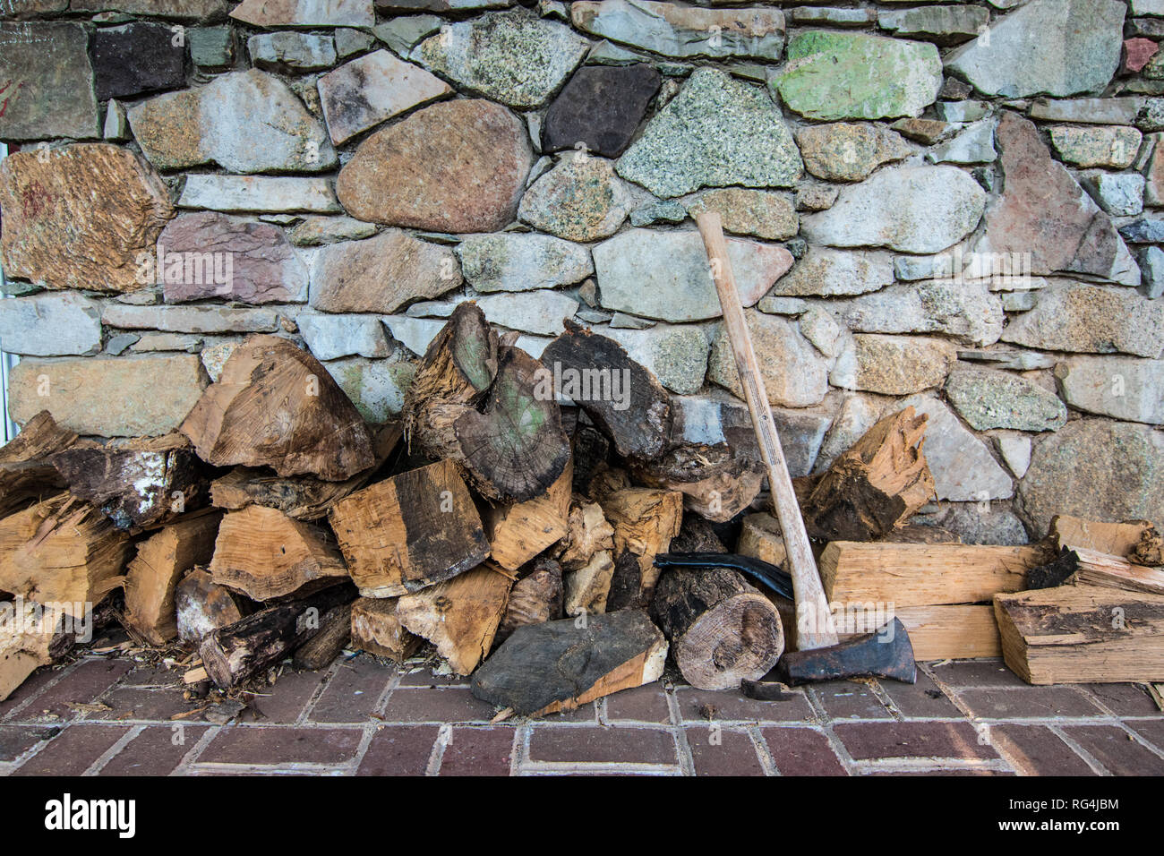 Firewood stocked next to Ax in front of Stone Wall Stock Photo